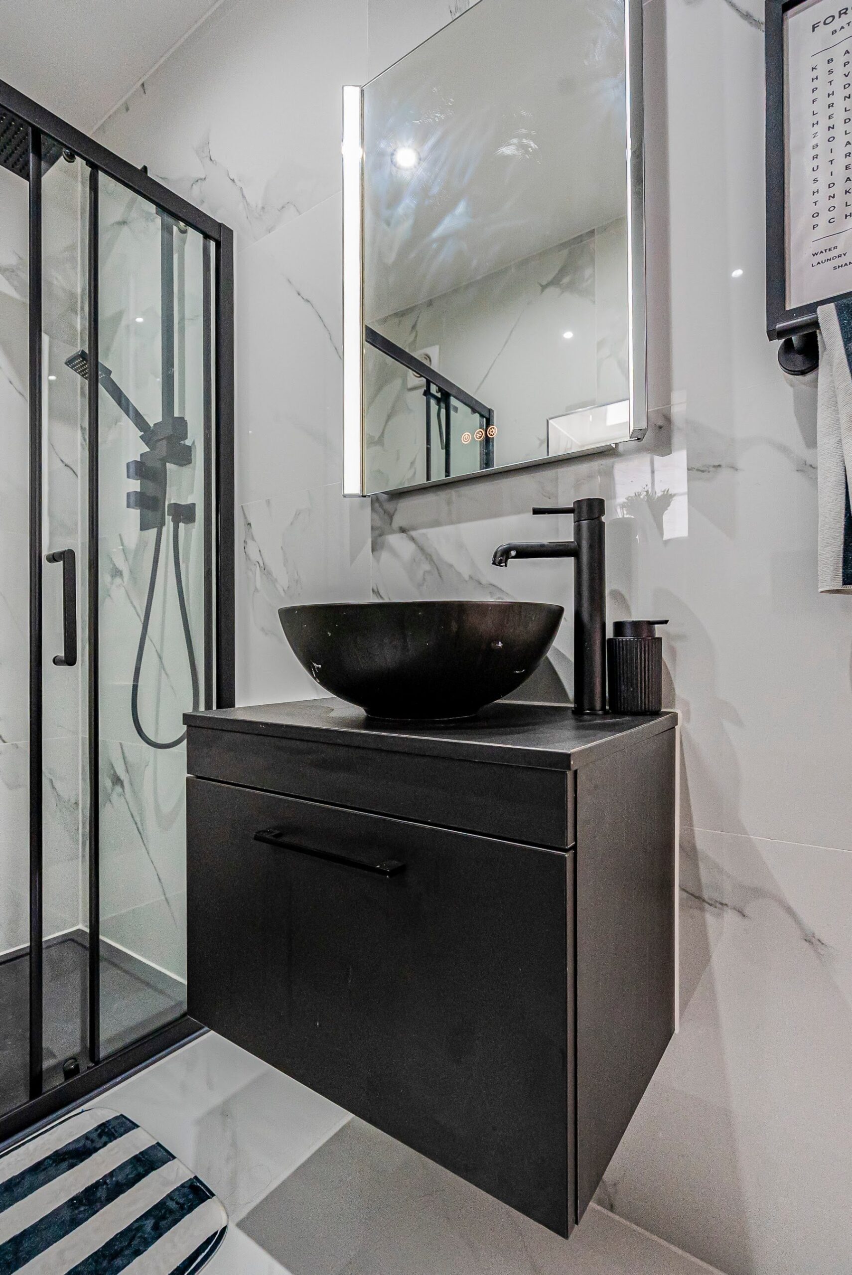 White marble-effect bathroom with black-framed shower glazing and a dark countertop basin
