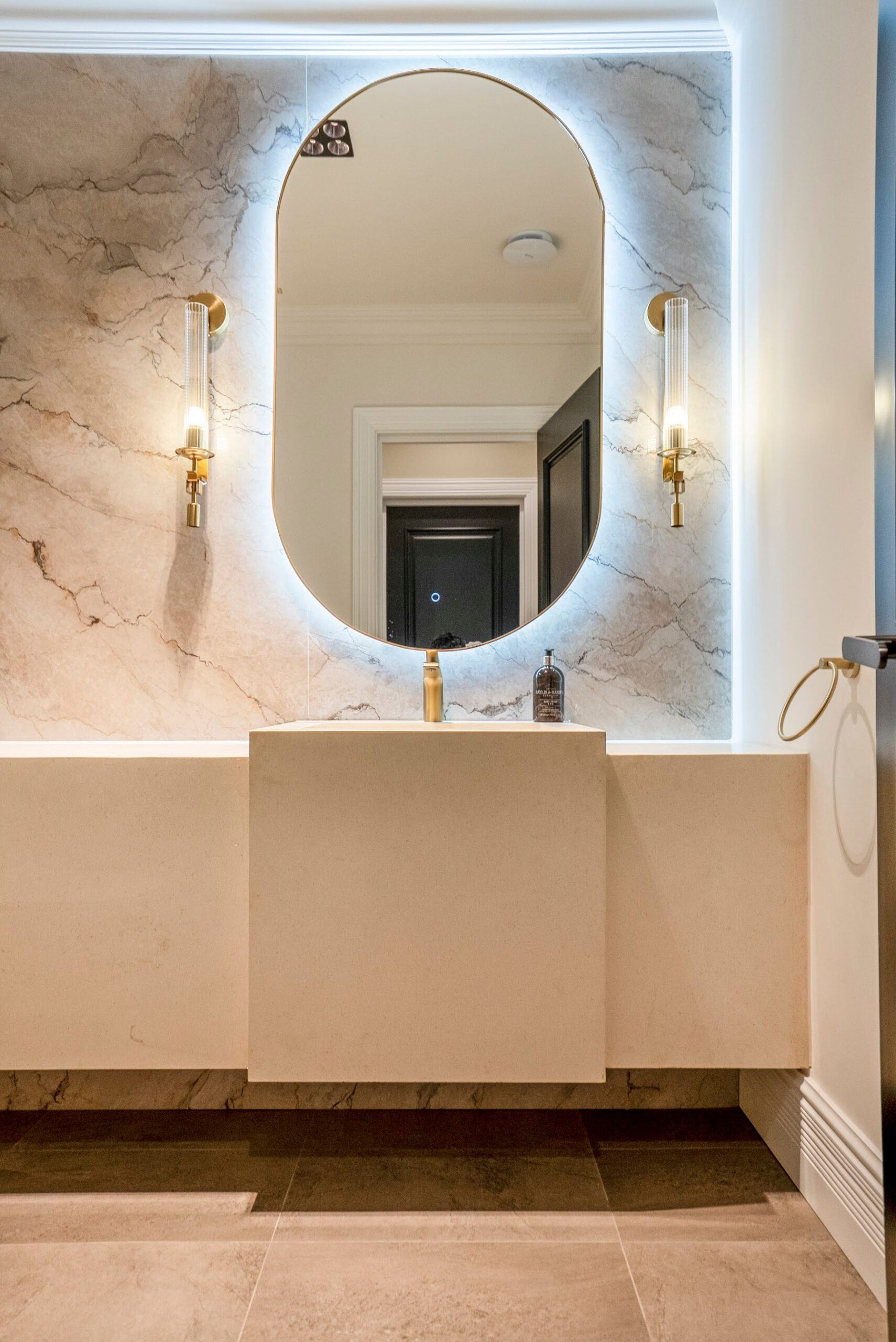 Bathroom with large-format marble-effect surfaces, a backlit mirror and brass wall lights